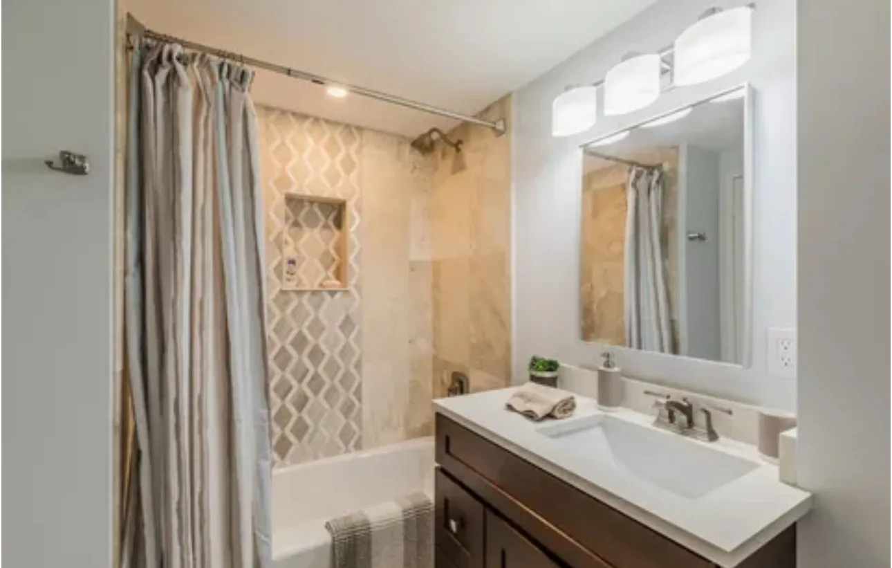 Bathroom with a tub and shower, a patterned curtain, a wood vanity and a wide mirror.