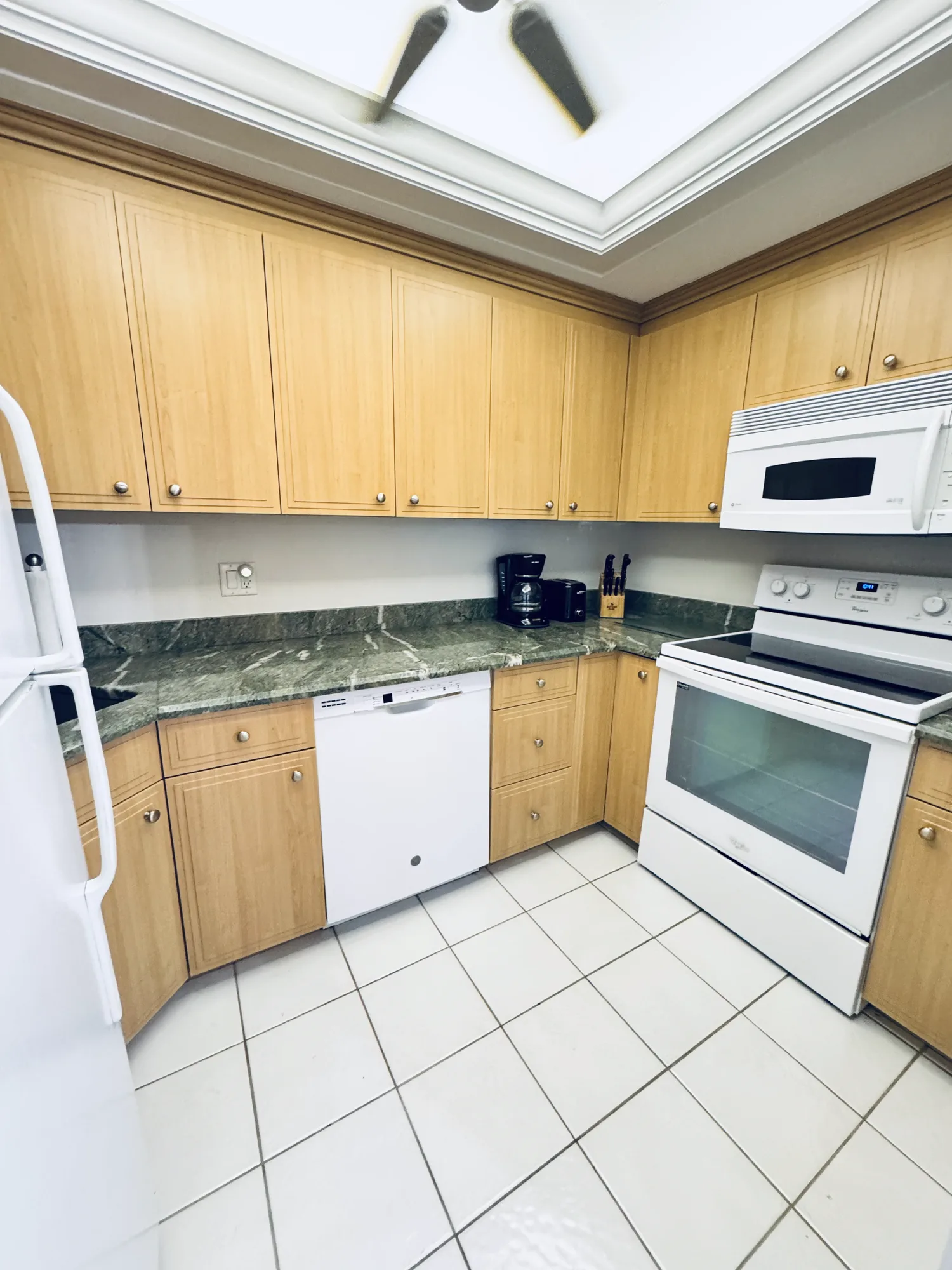 Kitchen with light wood cabinets, white appliances, green stone counters, and a tile floor.
