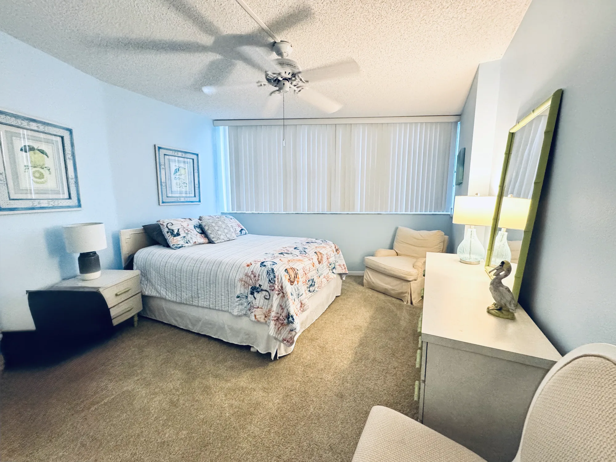 Bedroom with a bed in floral bedding, a bedside lamp, a ceiling fan, and windows with vertical blinds.
