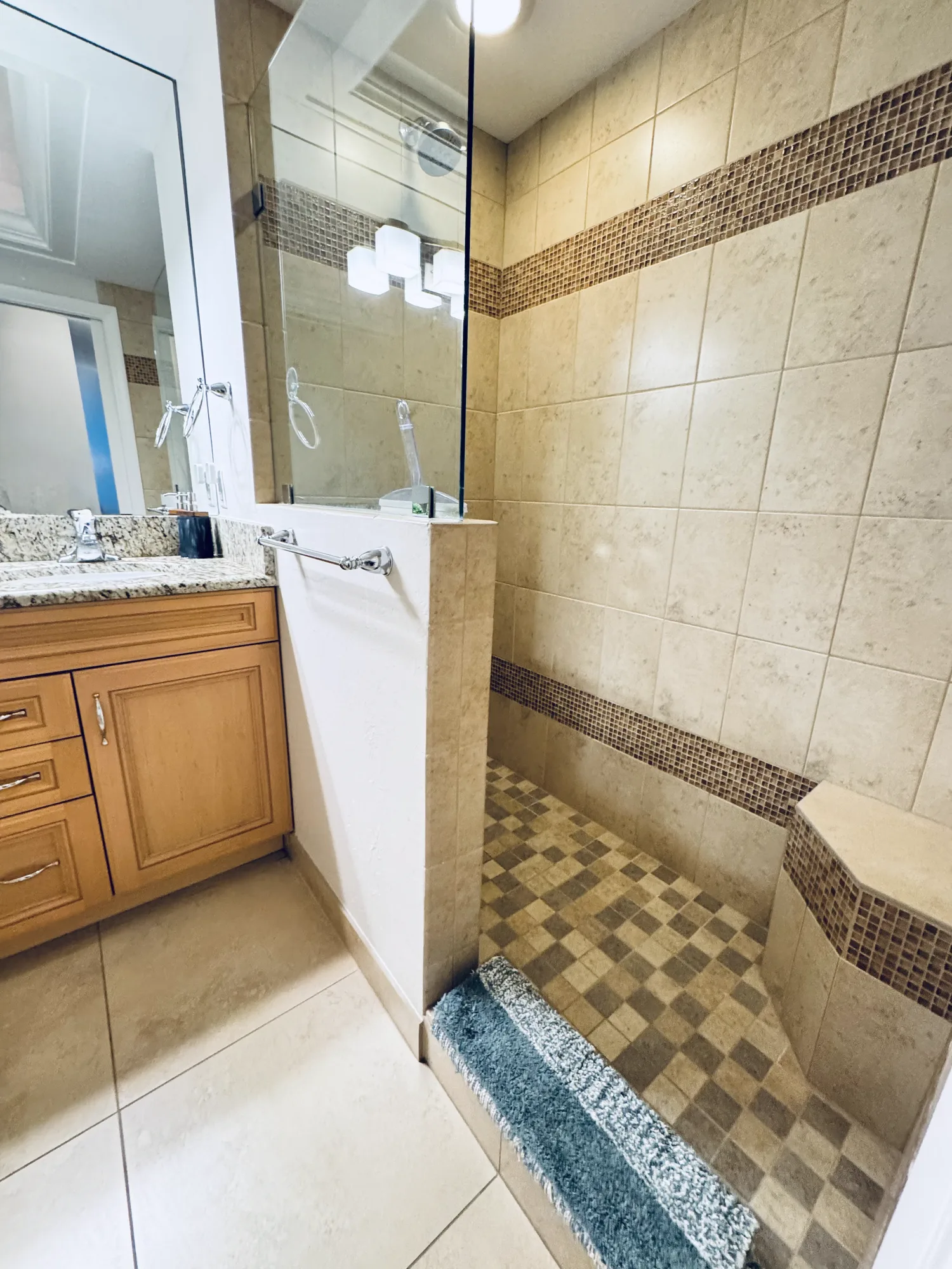 Walk-in shower with a glass door, beige tile and a mosaic tile border.