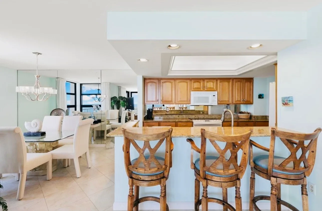 Kitchen with wood cabinets, stone counters, a breakfast bar with four wooden stools, and white appliances.