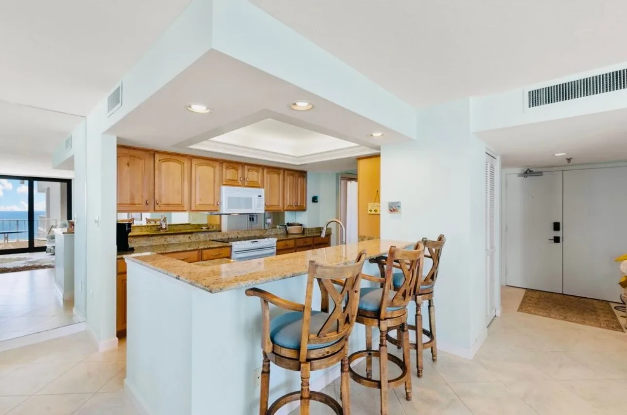 Open kitchen with wood cabinets and a breakfast bar with wooden stools, looking through to the dining area.