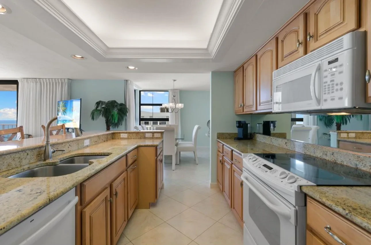 Kitchen with wood cabinets, stone counters, a white stove and microwave, and a window at the end.
