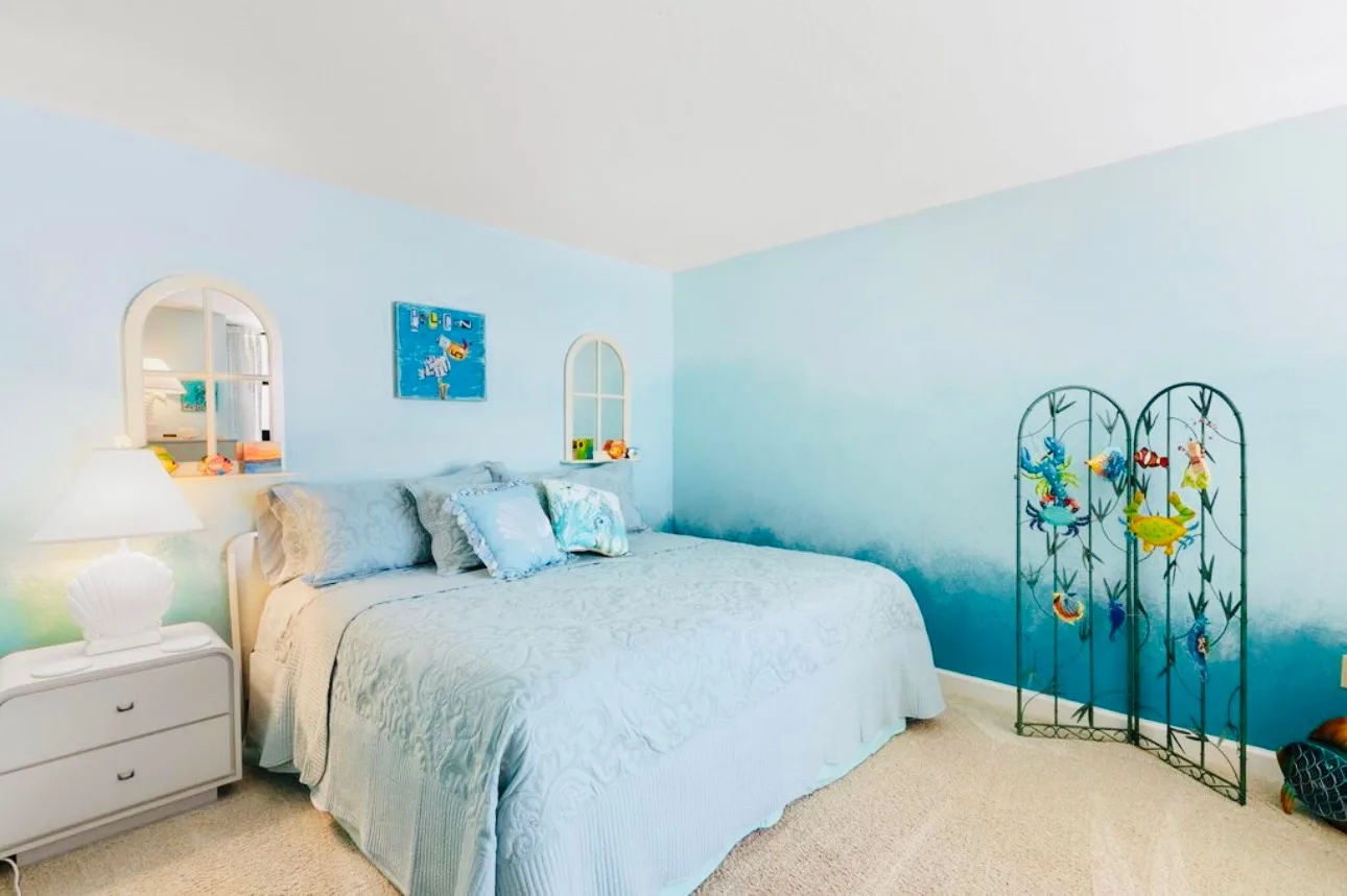 Second bedroom with pale blue walls, a bed with light blue bedding, a white dresser, and a decorative folding screen in the corner.