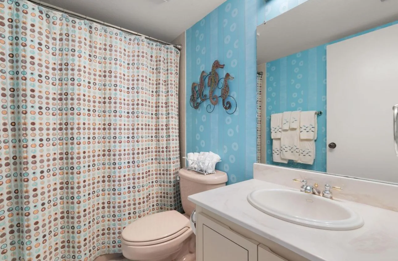 Second bathroom with light blue walls, a patterned shower curtain and a white vanity.